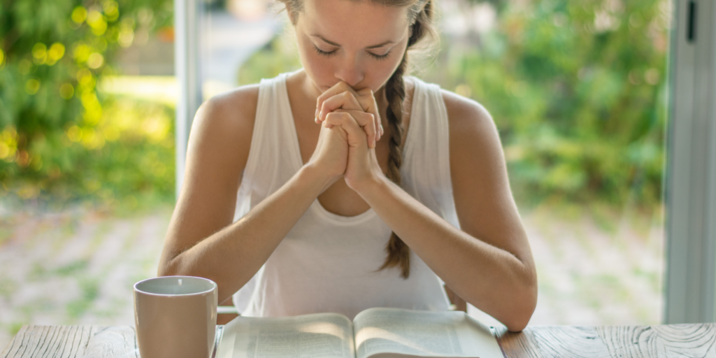 Woman at Table Praying Bible Hands folded 2400 x 1200